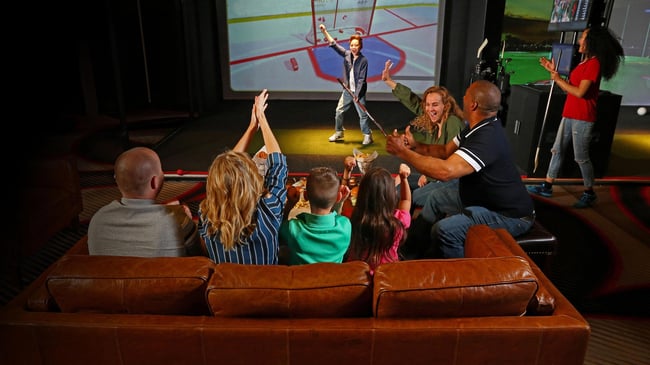 Family cheers as child plays an interactive hockey game on a large screen