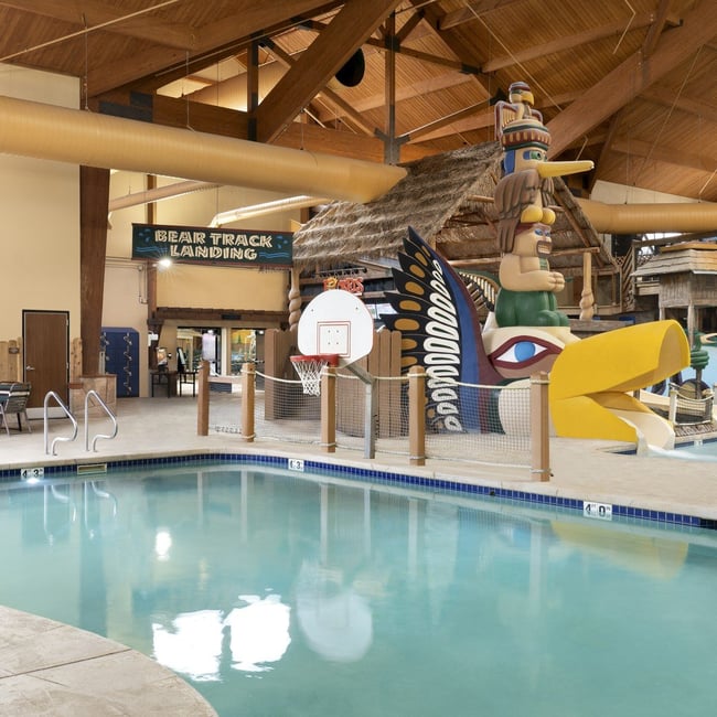 Indoor pool featuring a water slide and a basketball hoop for recreational activities.