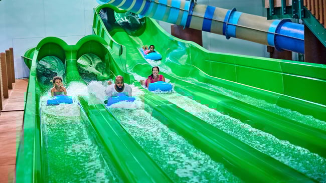 Guests race down a waterslide laying on a blue mat