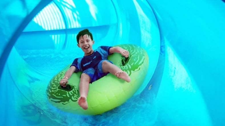 Boy rides down blue waterslide on green tube 