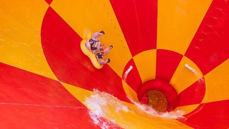 Four friends ride down a multicolored water slide in a tube 