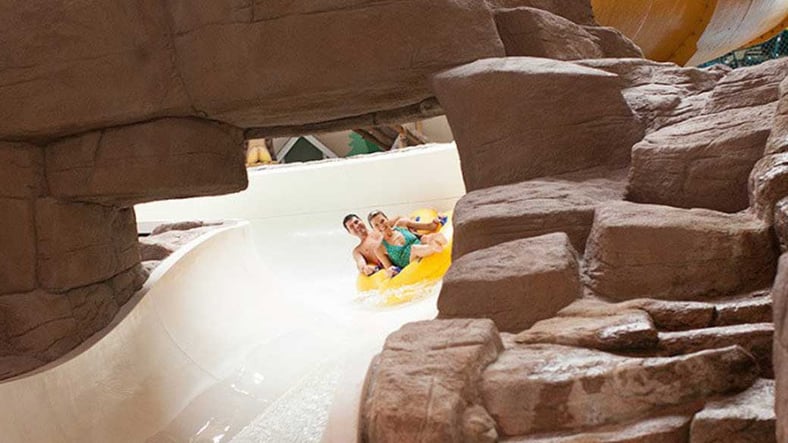 A couple in a tube race down the water slide surrounded by rock decor