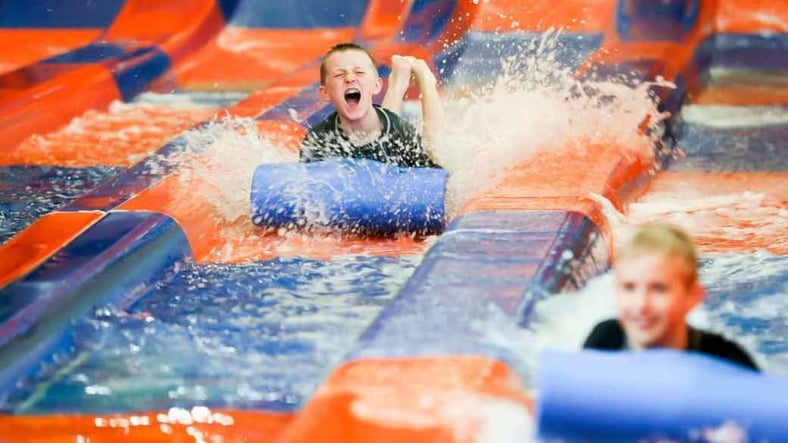 Two kids race down a waterslide laying on their stomaches 