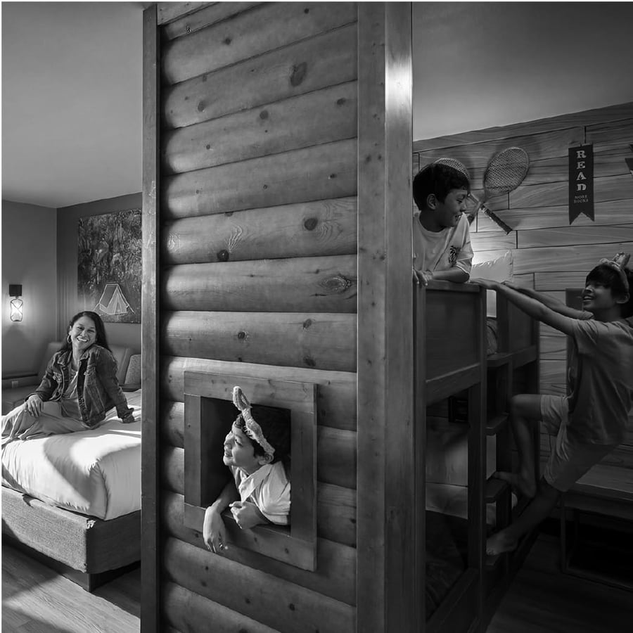 Three kids enjoying on a bunk bed in a themed suites as a mother sits in the main area smiling