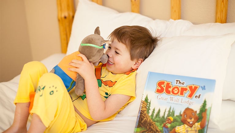 kid lying on bed holding a plush toy and a story book