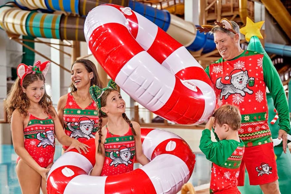 happy family wearing chrimstas themed swimwear smiling at each other as they play with swimming tubes
