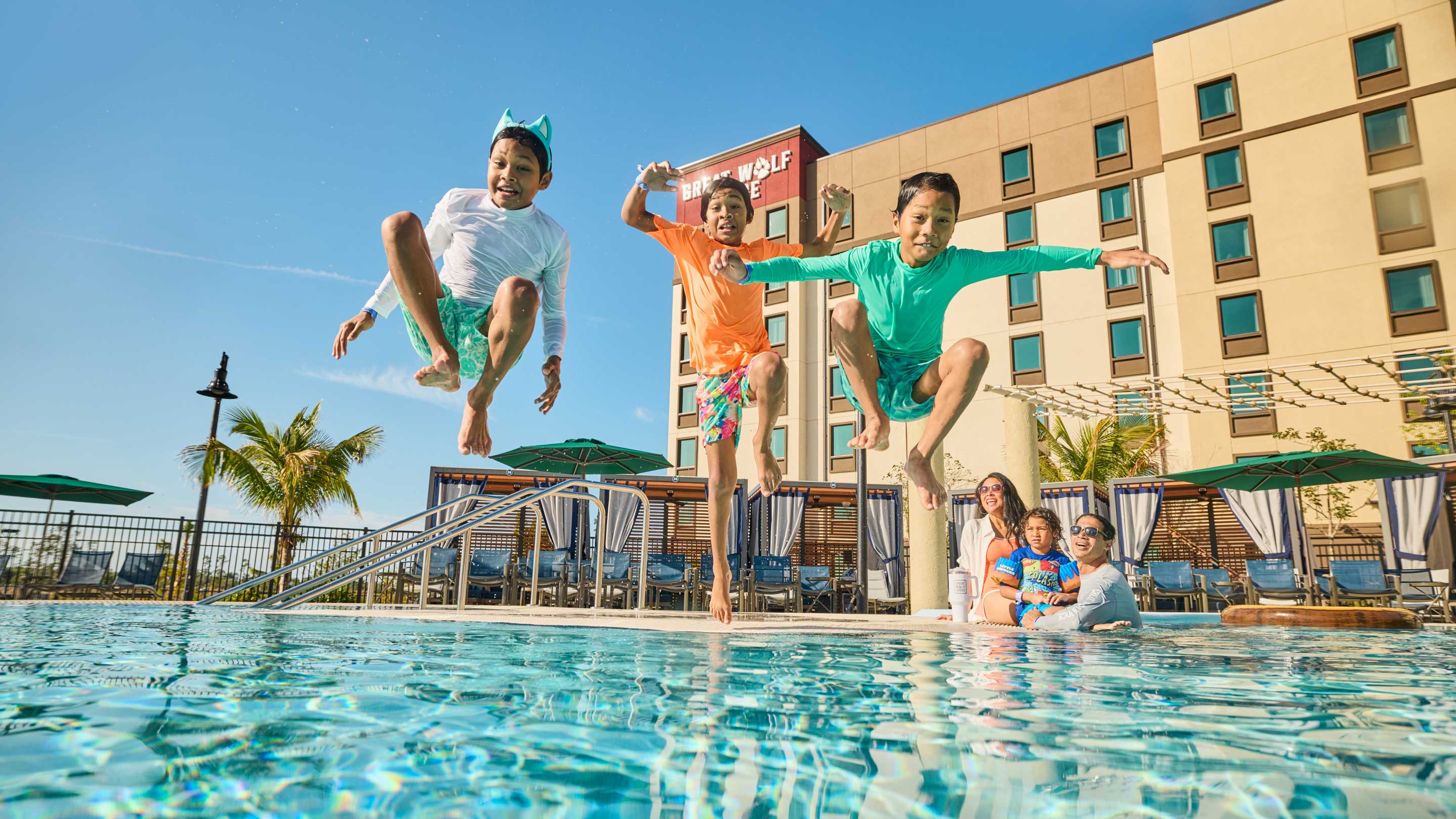 three boys jumping into the pool as mothers watch them