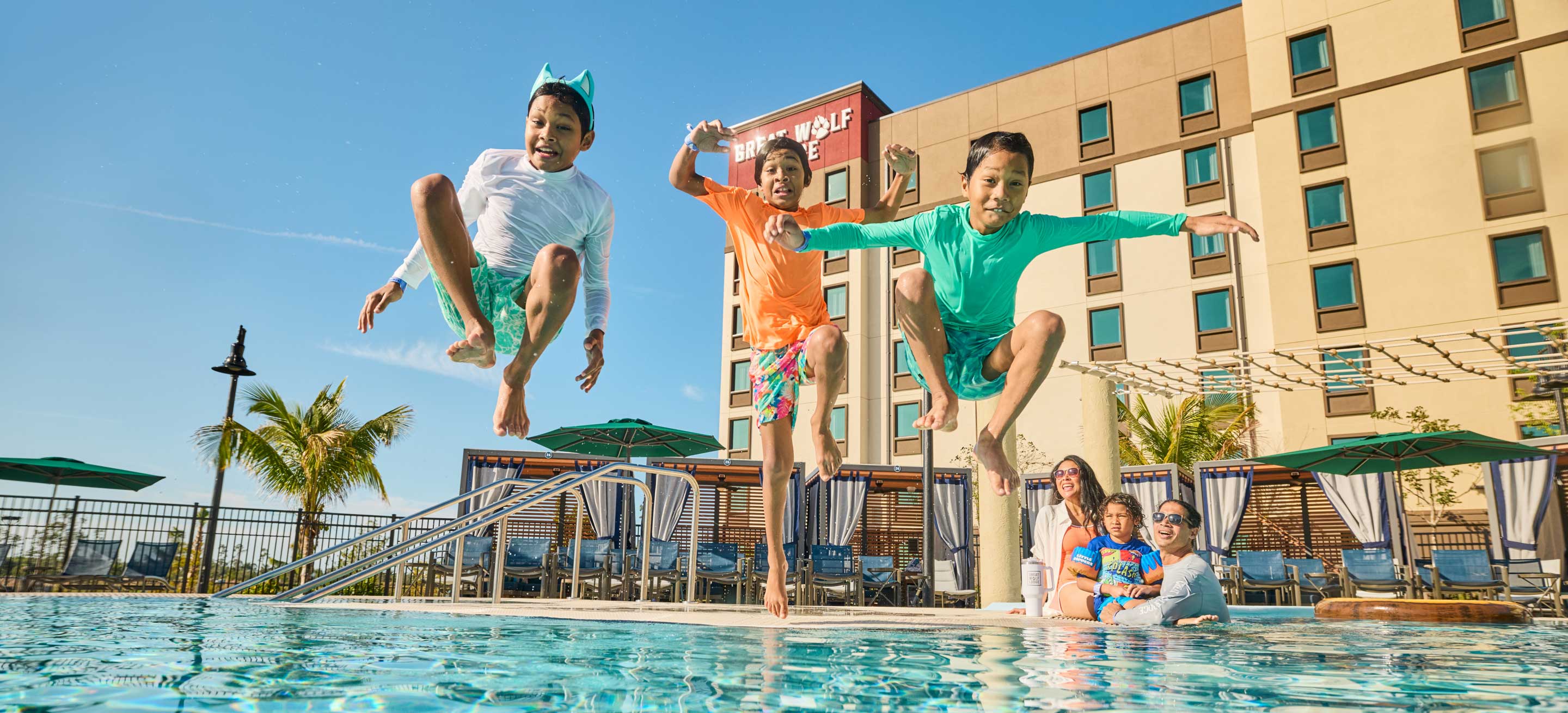 three boys jumping into the pool as mothers watch them