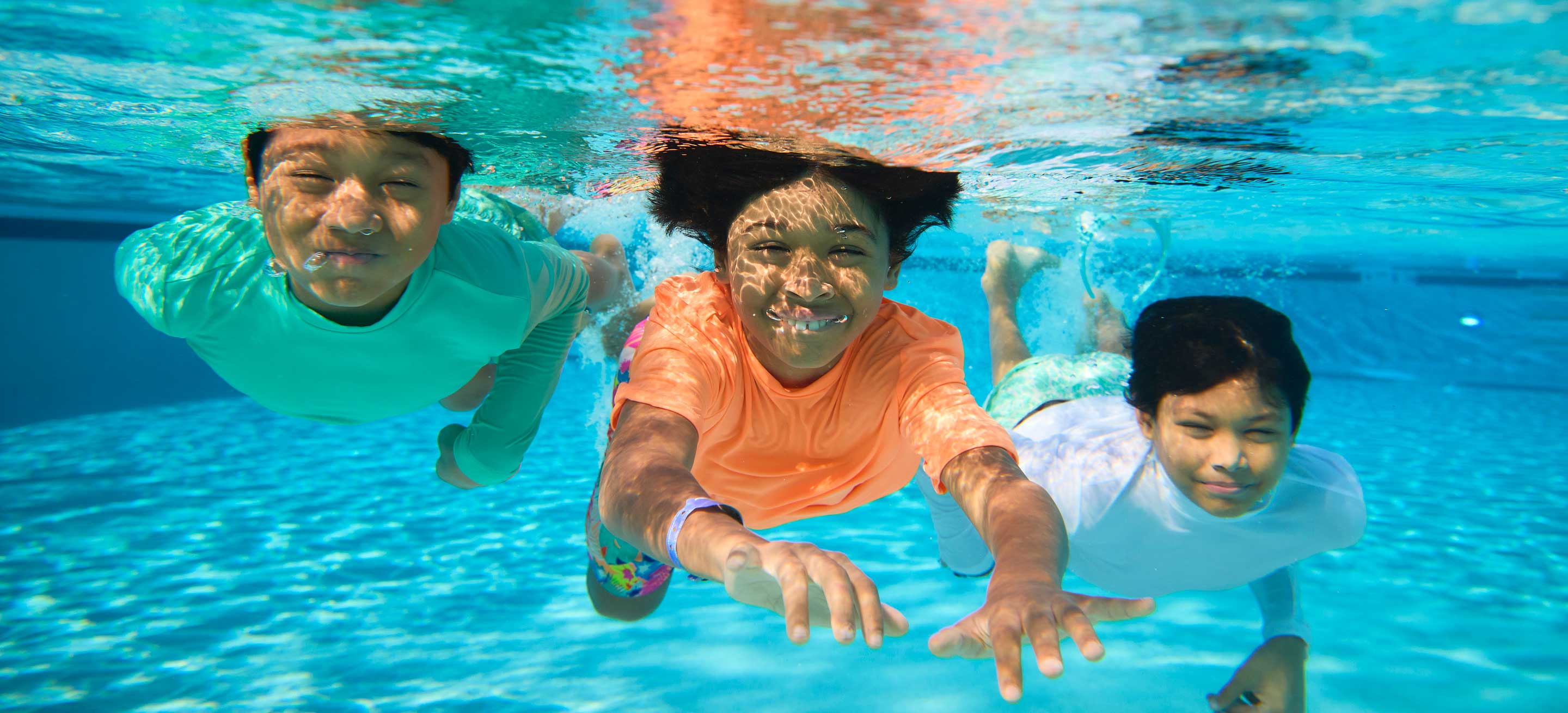three boys swimming under water in a pool
