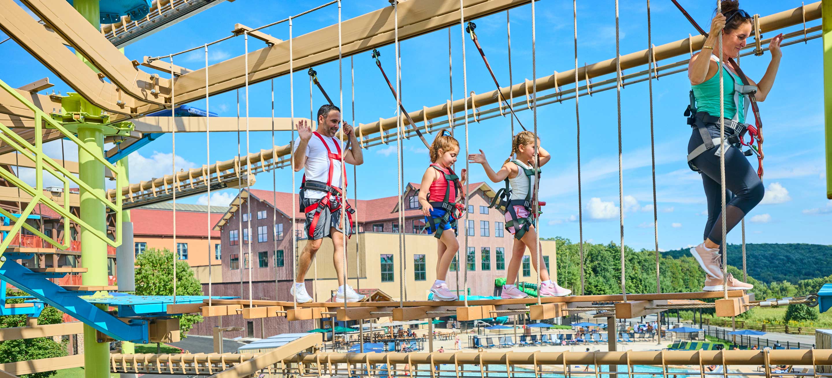 family crossing the rope course with pool in the background