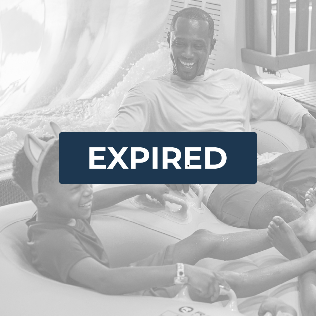 father looks at his son happily as they ride a tube on a water slide