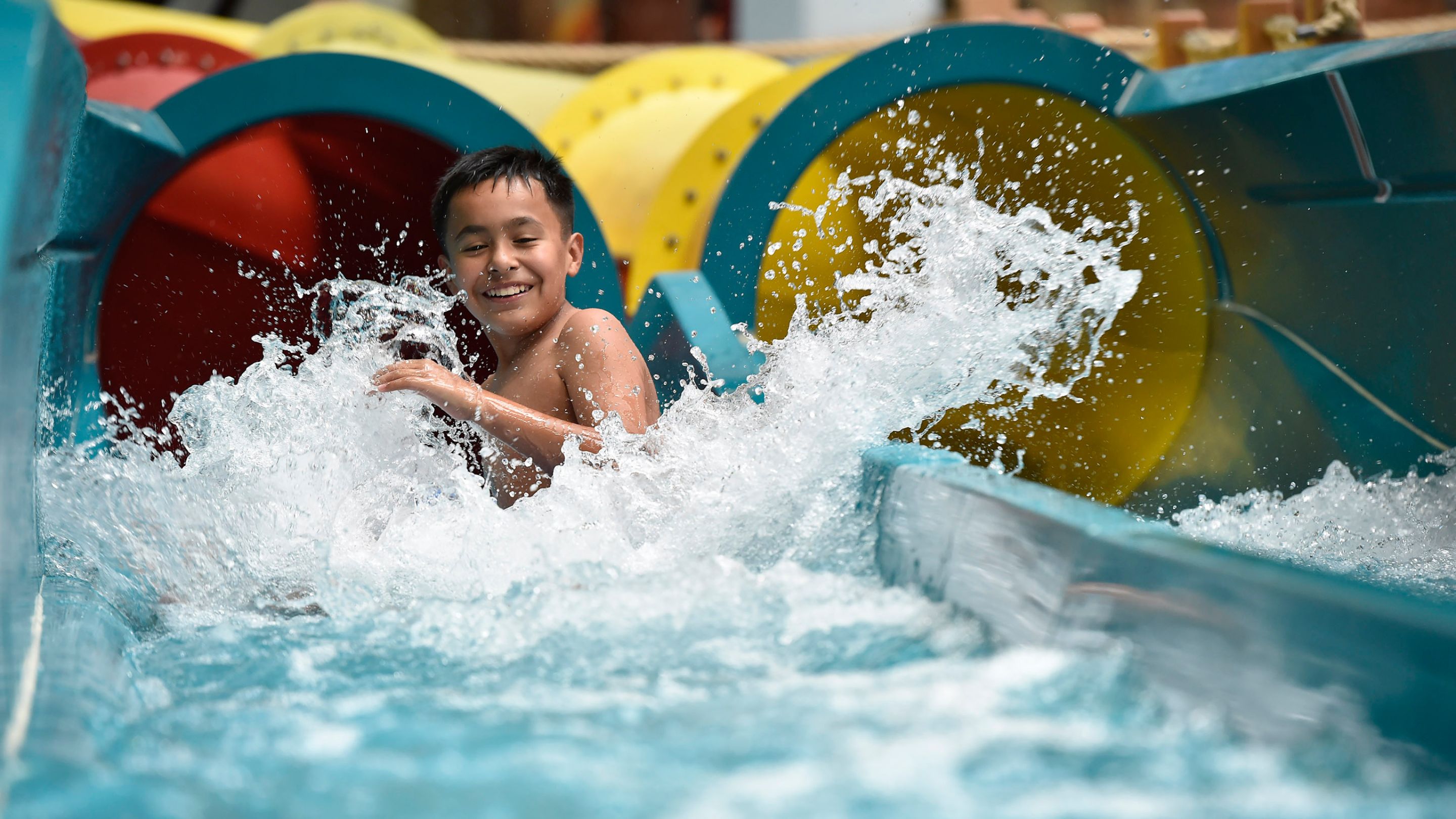 A young boy smiling as he splashes down a water slide into the landing pool.