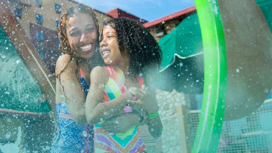mother hugging child under the spray of an attraction in the outdoor water park.