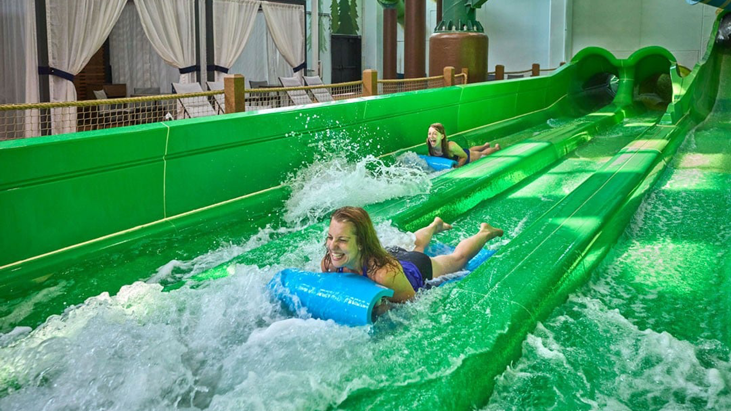 Mother and daughter sliding down an indoor green water slider at Great Wolf lodge