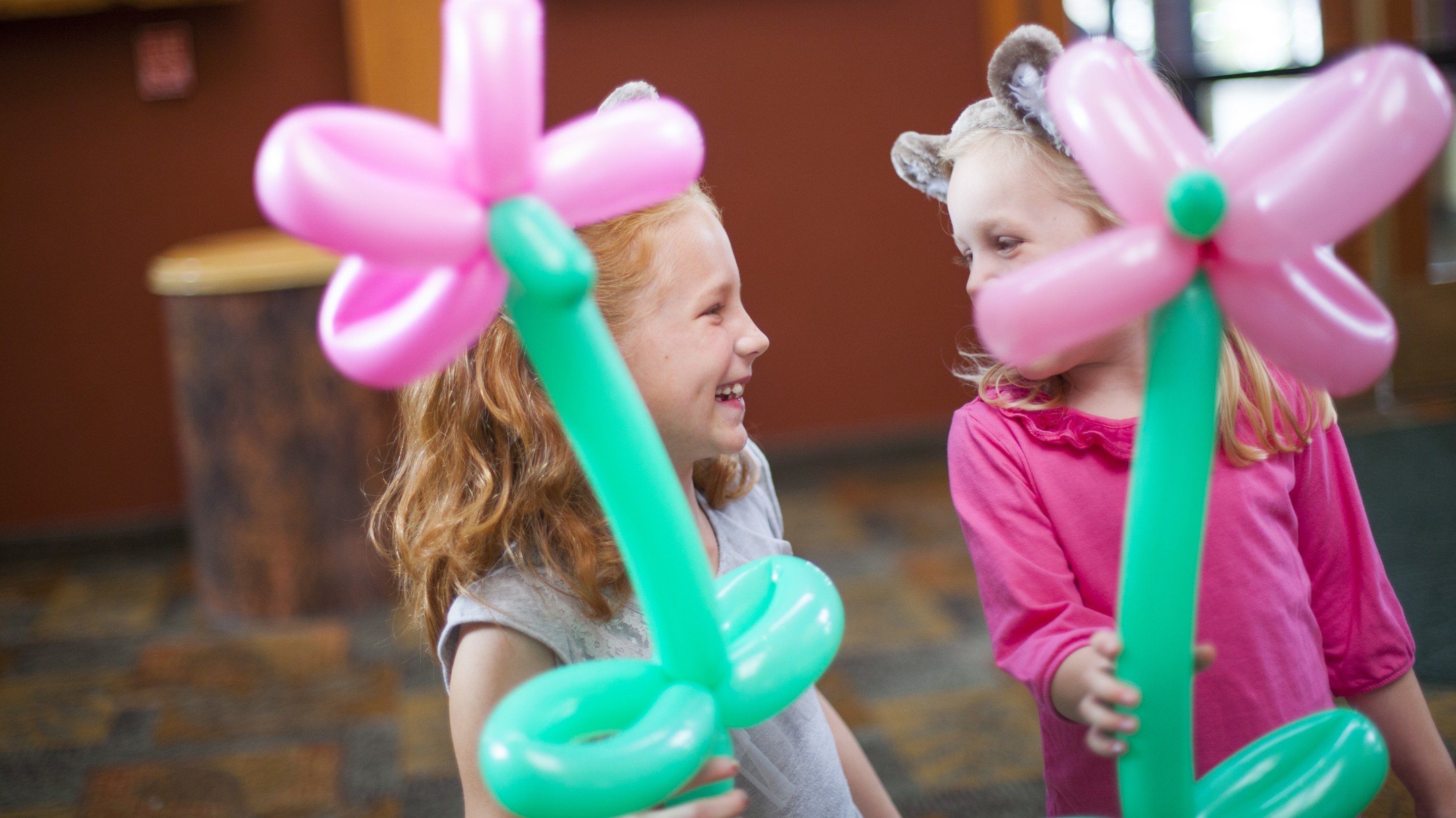 Two smiling girls holding balloon flowers indoors