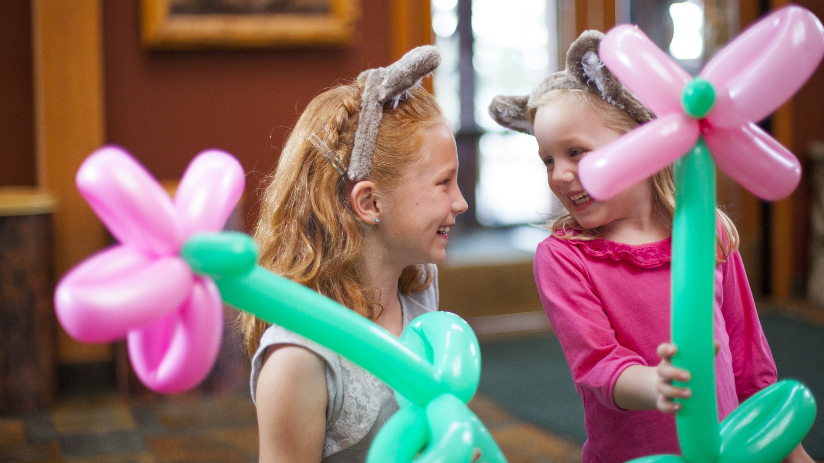 Two smiling girls holding twisted balloon flowers in hand