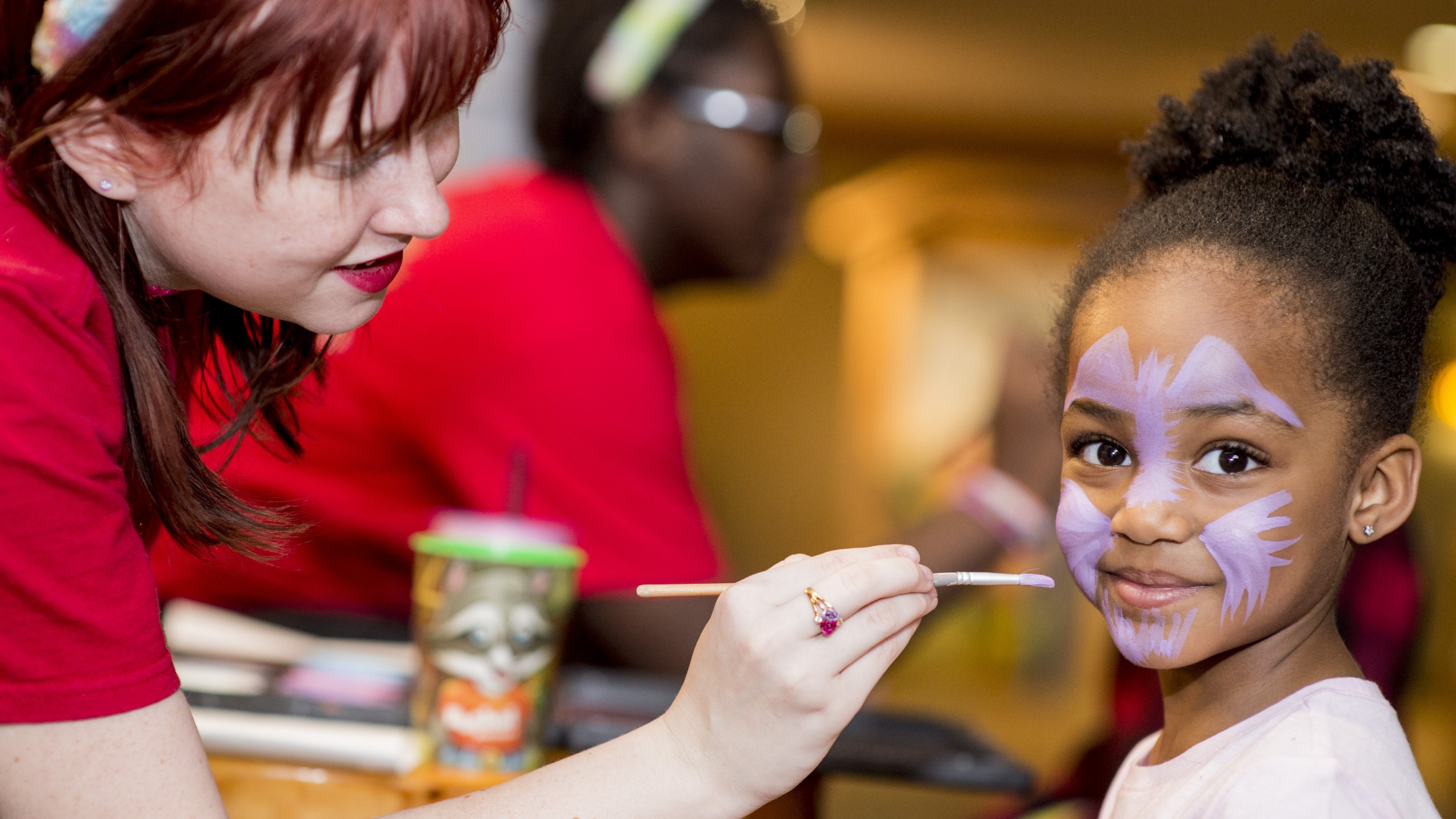 A young girl smiles while getting her face painted like a playful animal
