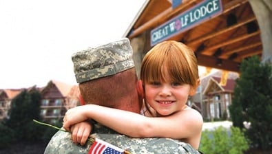 A father in military clothing holds his daughter who is smiling