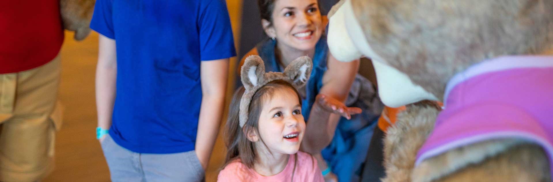 A girl wearing wolf ears looks up to a Great Wolf Lodge character.