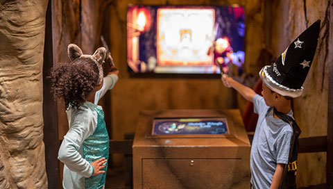 girl in wolf ears and boy in wizard hat raise their wands to play MagiQuest game