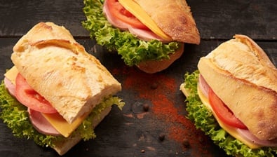 Three sandwiches filled with lettuce, tomato, cheese and turkey lay next to each other on a spice sprinkled wooden counter.