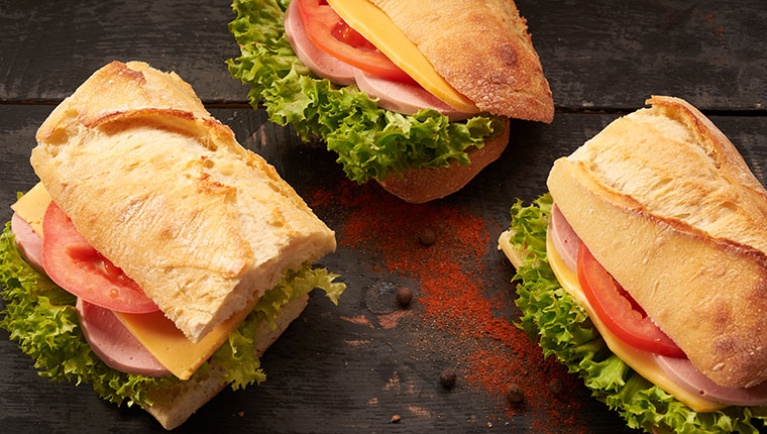 Three sandwiches filled with lettuce, tomato, cheese and turkey lay next to each other on a spice sprinkled wooden counter 