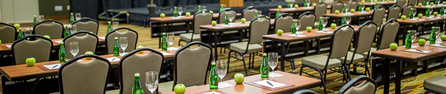 chairs and tables with water and apples on it face a stage