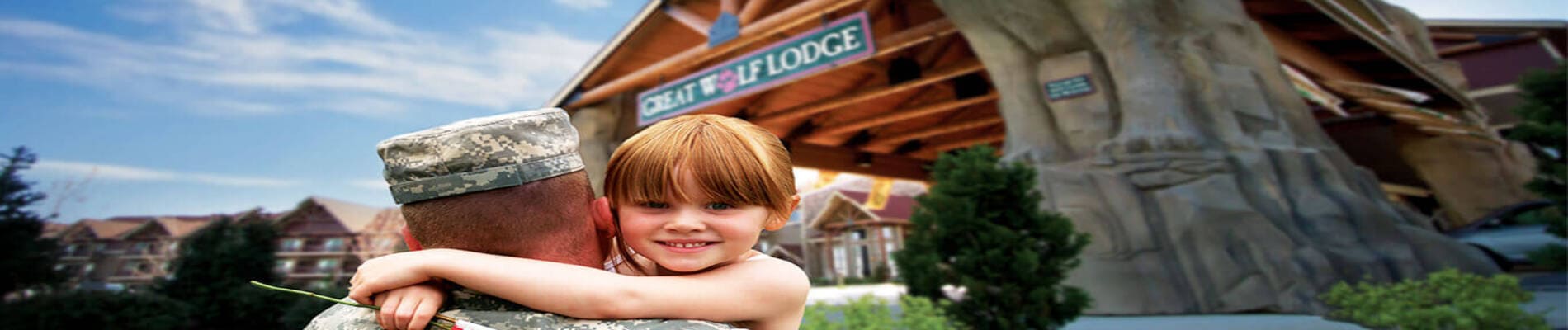 A girl smiles at the camera as her military father carries her toward a Great Wolf Lodge indoor water park and resort.