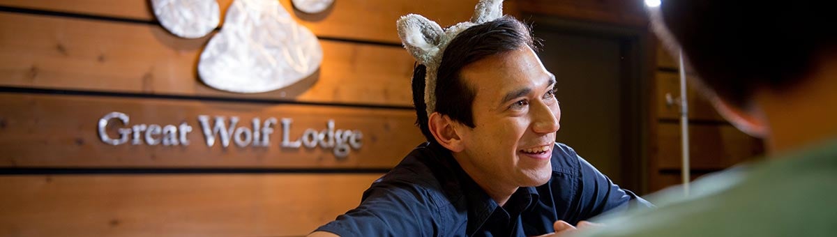employee wears wolf ears as he helps guests at front desk of resort.