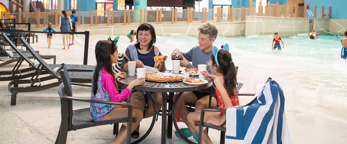 A family enjoy pizza and drinks in their own private seating at Great Wolf Lodge indoor water park and resort.