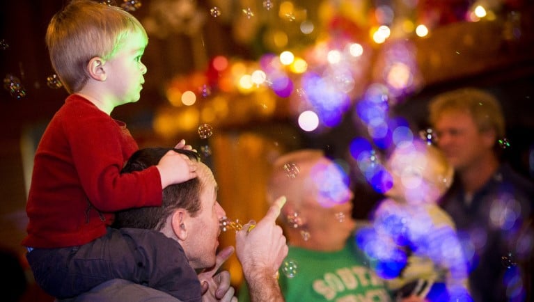 son sits on dad's shoulders as they play in bubbles