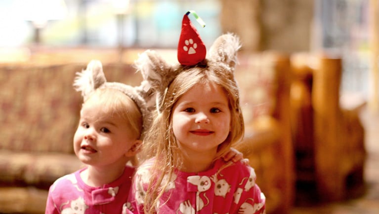 Two young children smile at the camera while wearing pajamas and wolf ears at Great Wolf Lodge.