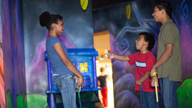 A family of three play Howl at the Moon Glow Golf at Great Wolf Lodge indoor water park and resort.