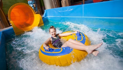 Boy rides down blue waterslide on green tube 