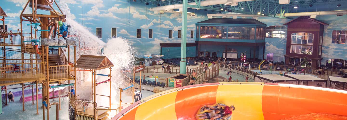 families play on jungle gym and yellow and orange slide in indoor water park