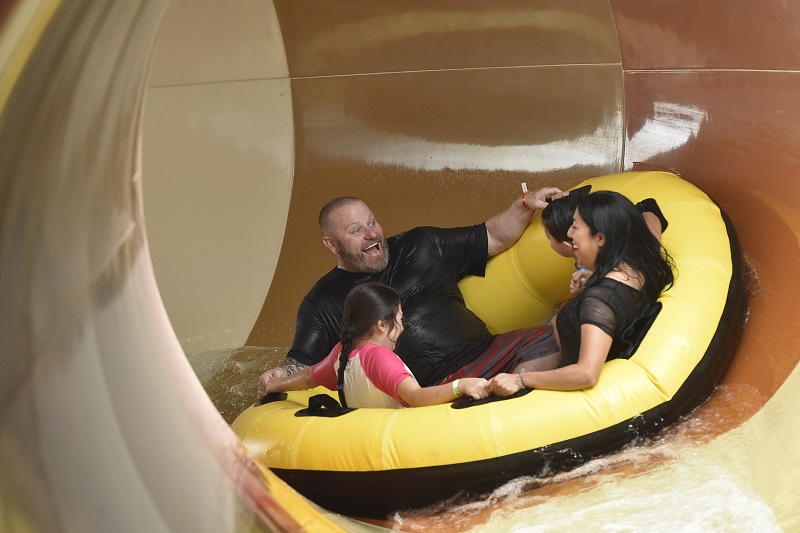 Parents and children ride down a waterslide in a yellow tube