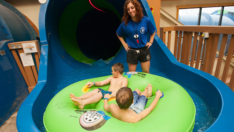 A lifeguard watches as two boys enter the Double Barrel Drop water slide