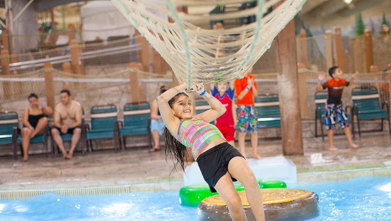 A girl balances herself on a cargo net in the Frog Bog Log Walk pool at Great Wolf Lodge indoor water park and resort.