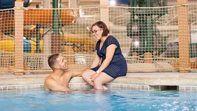 A couple relax in and on the side of the indoor pool 