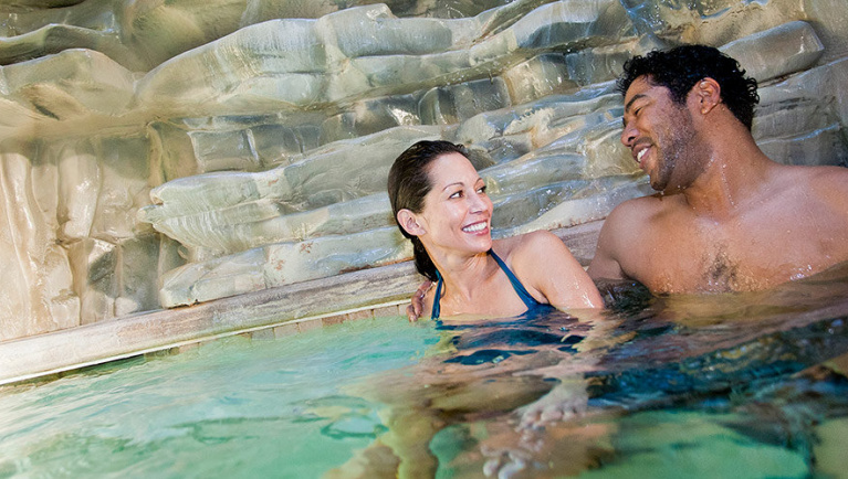 A couple relax by the pool at the Northwoods Oasis area