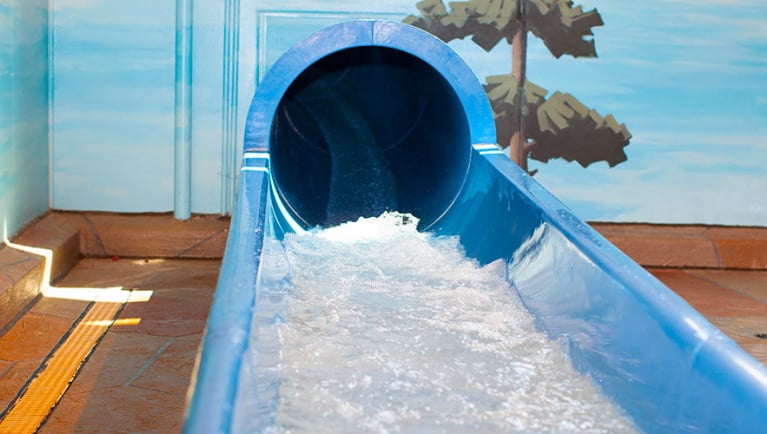 The end of a blue waterslide with water splashing out