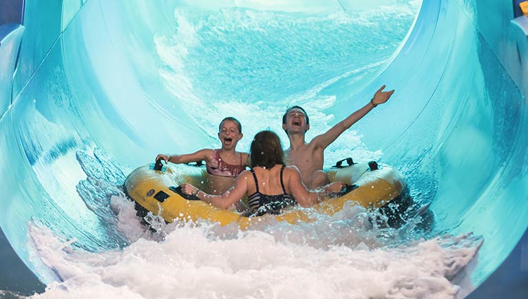 A family of three shares a tube down River Canyon Run at Great Wolf Lodge indoor water park and resort.
