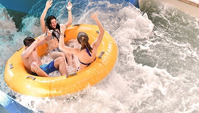 Dad and two kids laugh as they ride down a blue waterslide in a yellow tube 