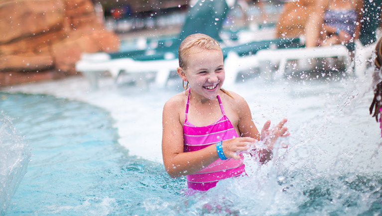 A girl splashes water in an outdoor pool at Great Wolf Lodge indoor water park and resort.