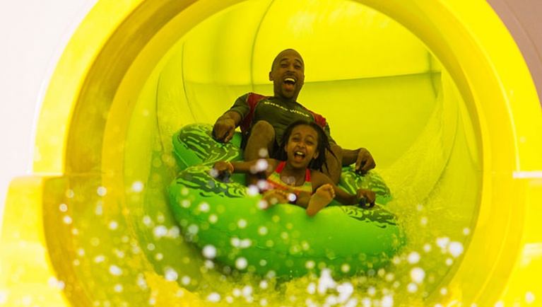 Dad and daughter ride down yellow waterslide in green tube