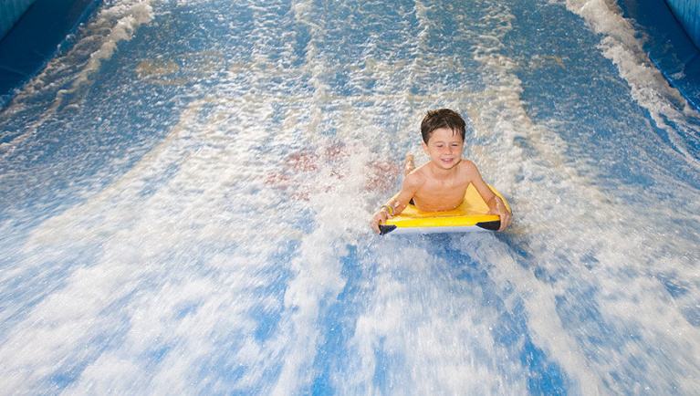 A boy balances on a bodyboard on Wolf Rider Wipeout at Great Wolf Lodge indoor water park and resort.