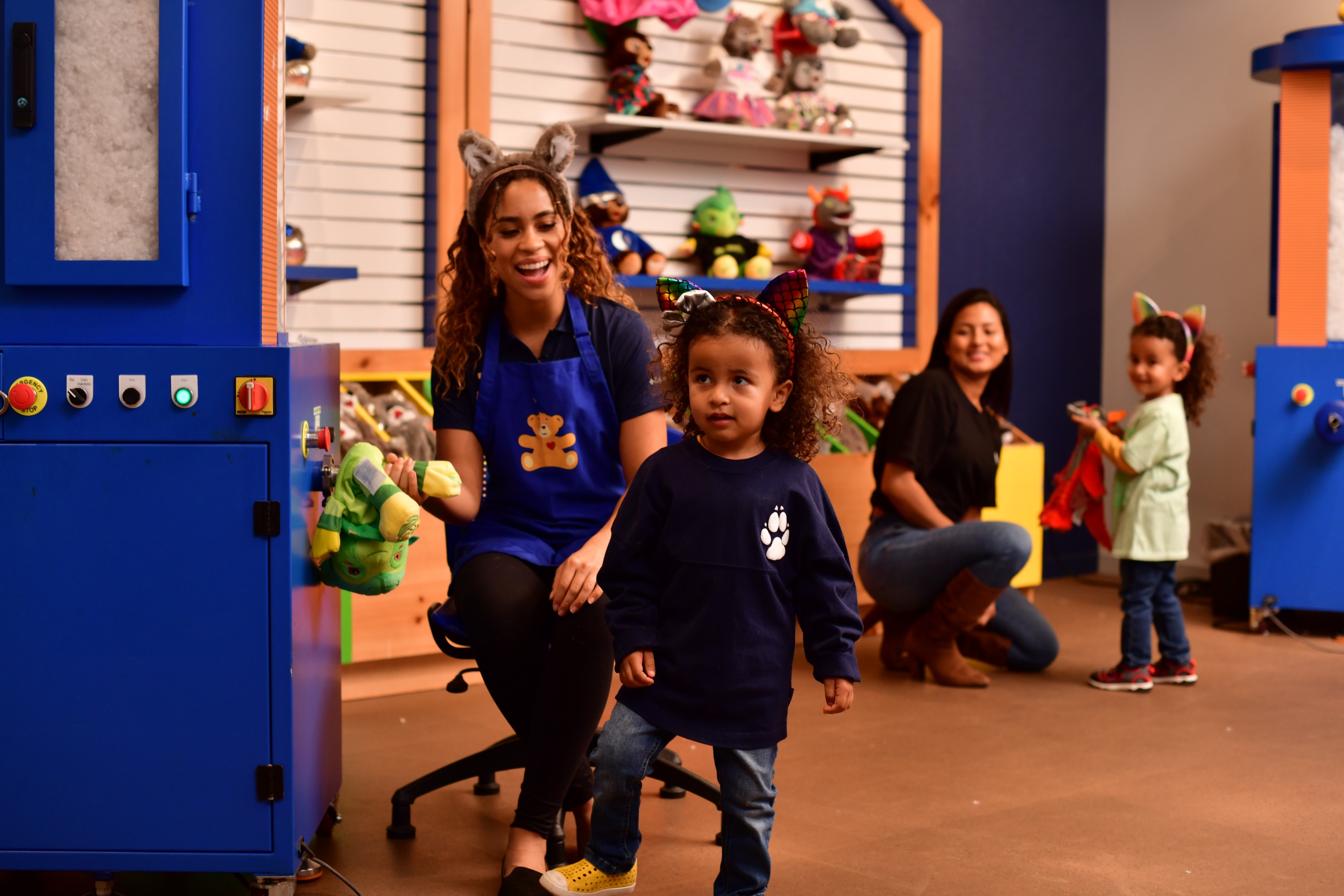 mothers and 2 girls watch as staff member stuffs a toy bear