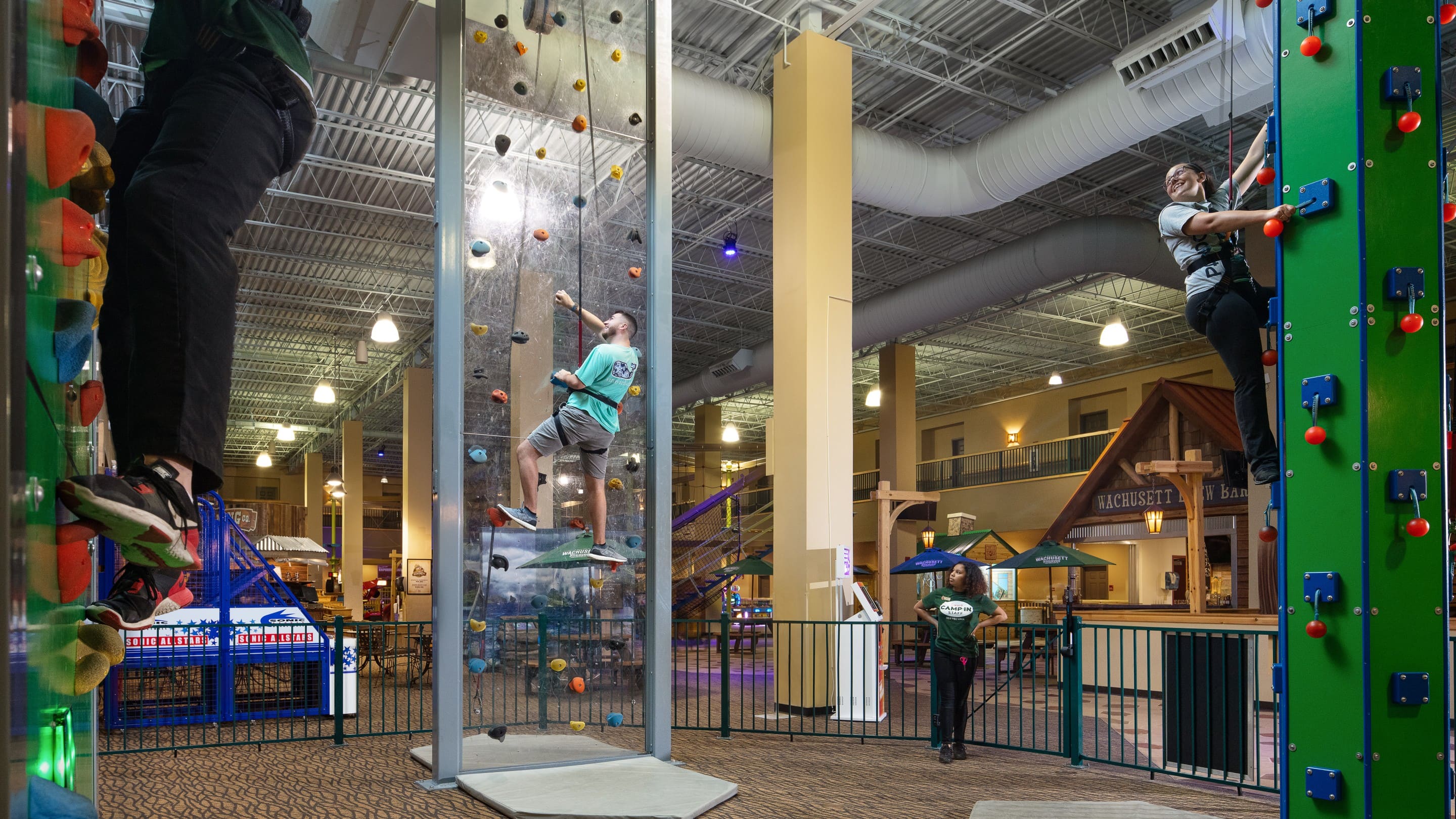Family climbing an indoor rock wall with safety harnesses