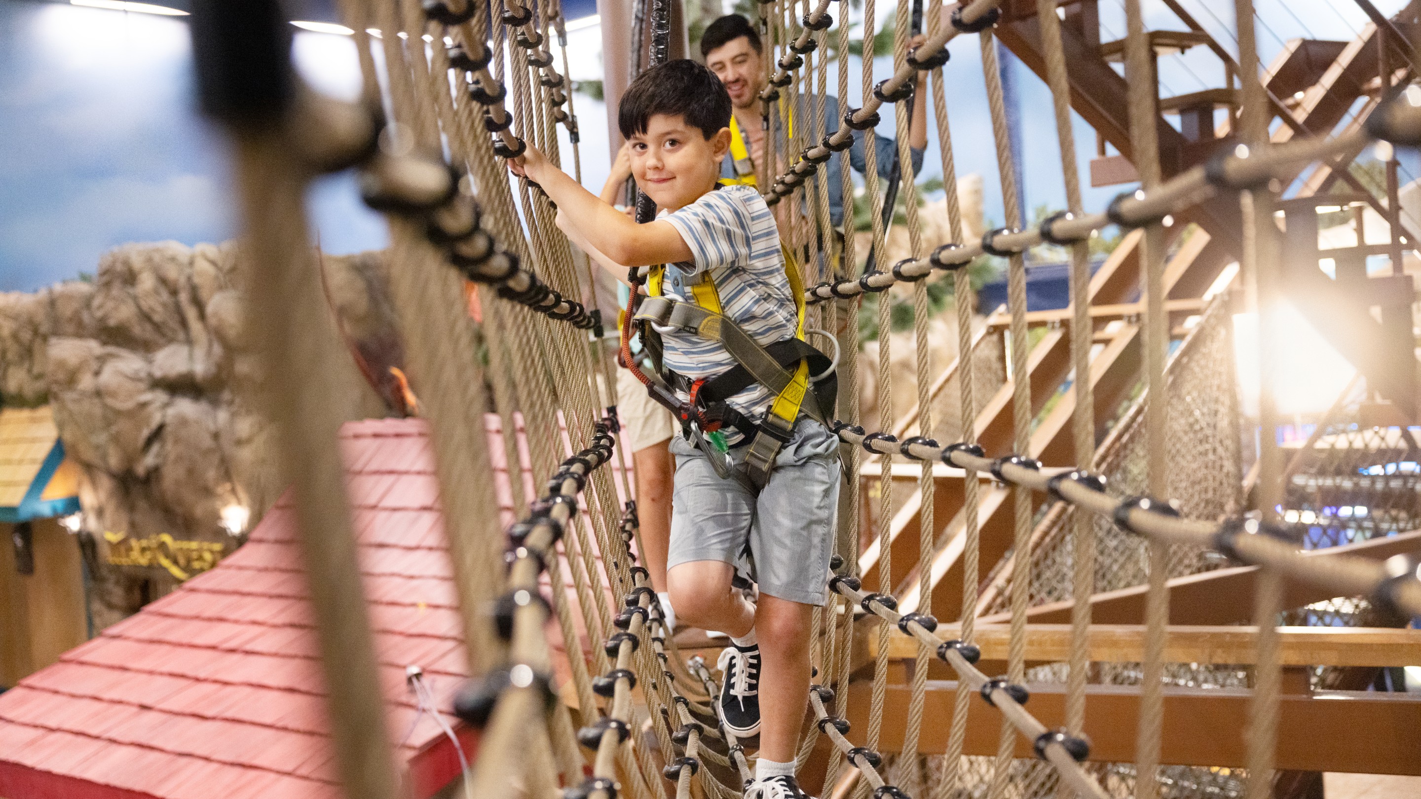 Boy crossing rope bridge at indoor adventure course