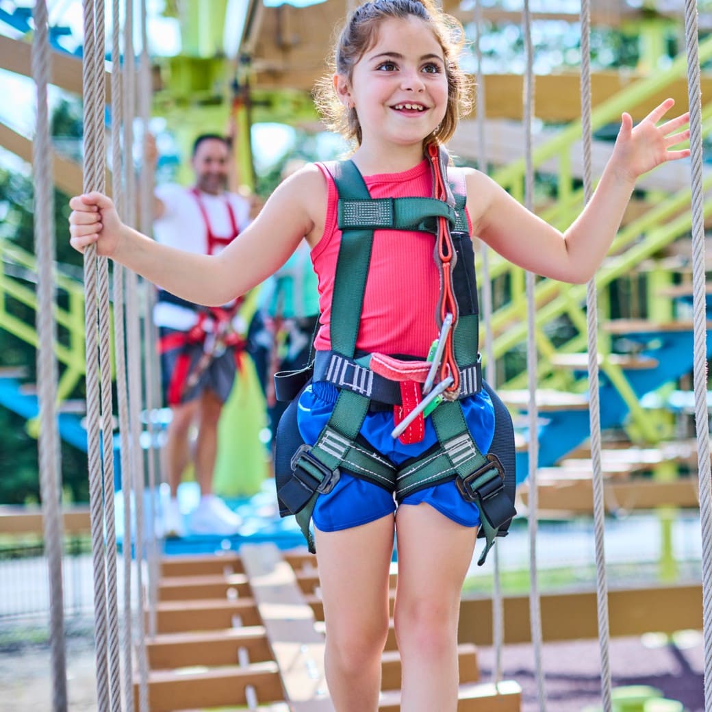Smiling girl in harness on a rope bridge